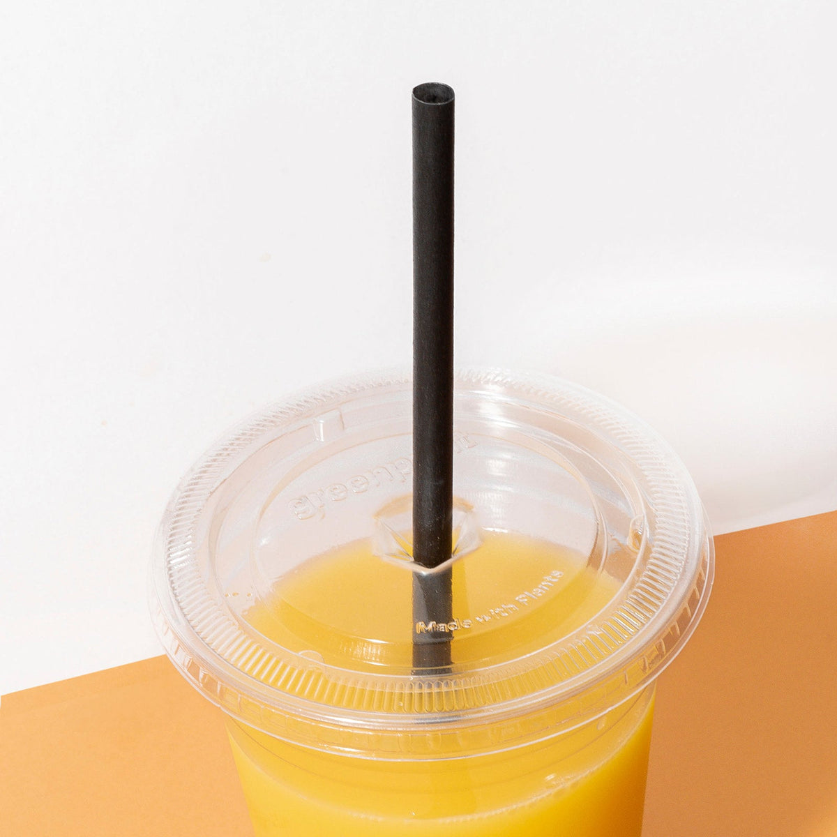 Clear compostable lid on a cup with yellow liquid and black straw on a white background