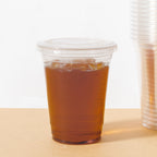 Clear compostable cup with lid with brown liquid on a beige surface