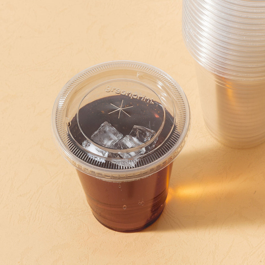 Clear plastic cup with lid with iced drink on a beige surface