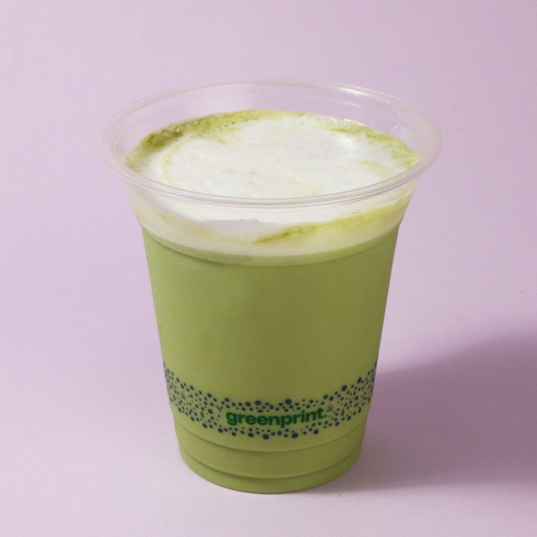 Green smoothie in a clear compostable plastic cup with 'greenprint' branding on a light purple background