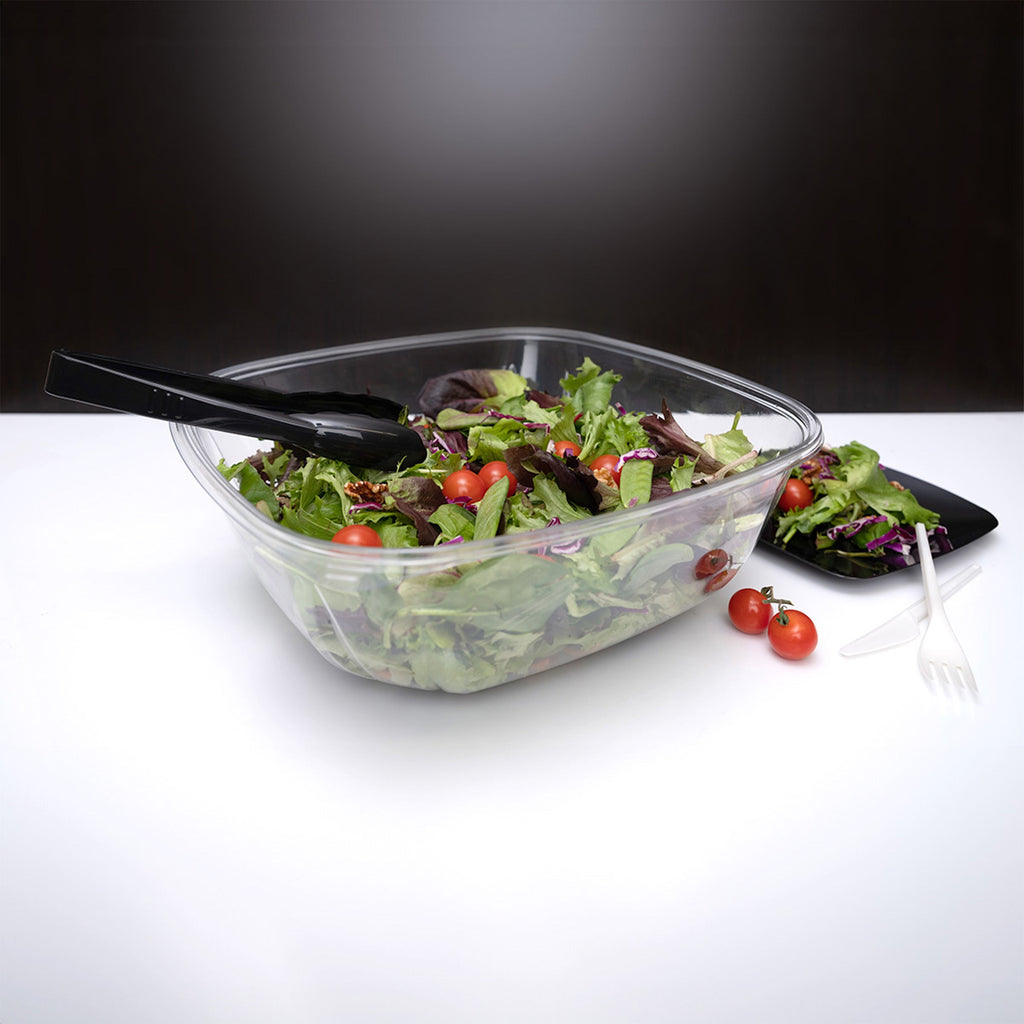Clear plastic container with salad and black utensils on a white surface