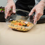Person in gloves closing a bowl with a lid of pasta salad on a beige surface