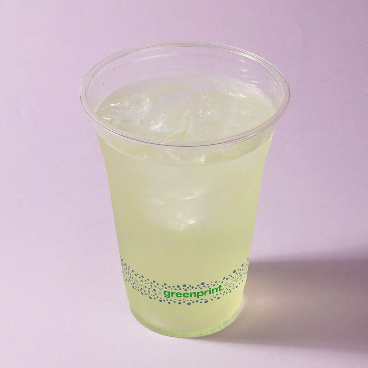Clear cold cup with yellow drink and 'greenprint' branding on a light purple background