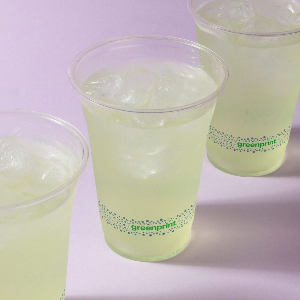 Three clear compostable cups filled with a green drink and ice, branded 'greenprint', on a light purple background.