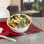 Disposable bowl of salad with a clear lid on a red cloth, blurred background