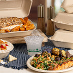 Plated food items including a sandwich, salad, and fries on a table with compostable containers and a cup.