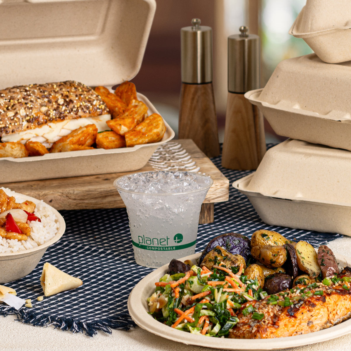 Plated food items including a sandwich, salad, and fries on a table with compostable containers and a cup.