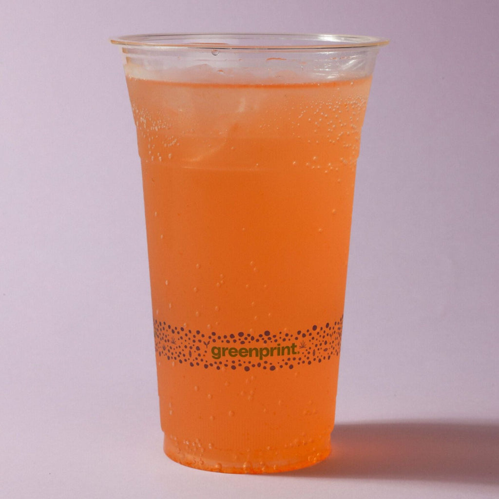 Clear cup with orange beverage and 'greenprint' logo on a light purple background