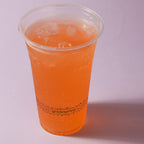 Clear compostable cup with orange beverage and ice on a light purple background