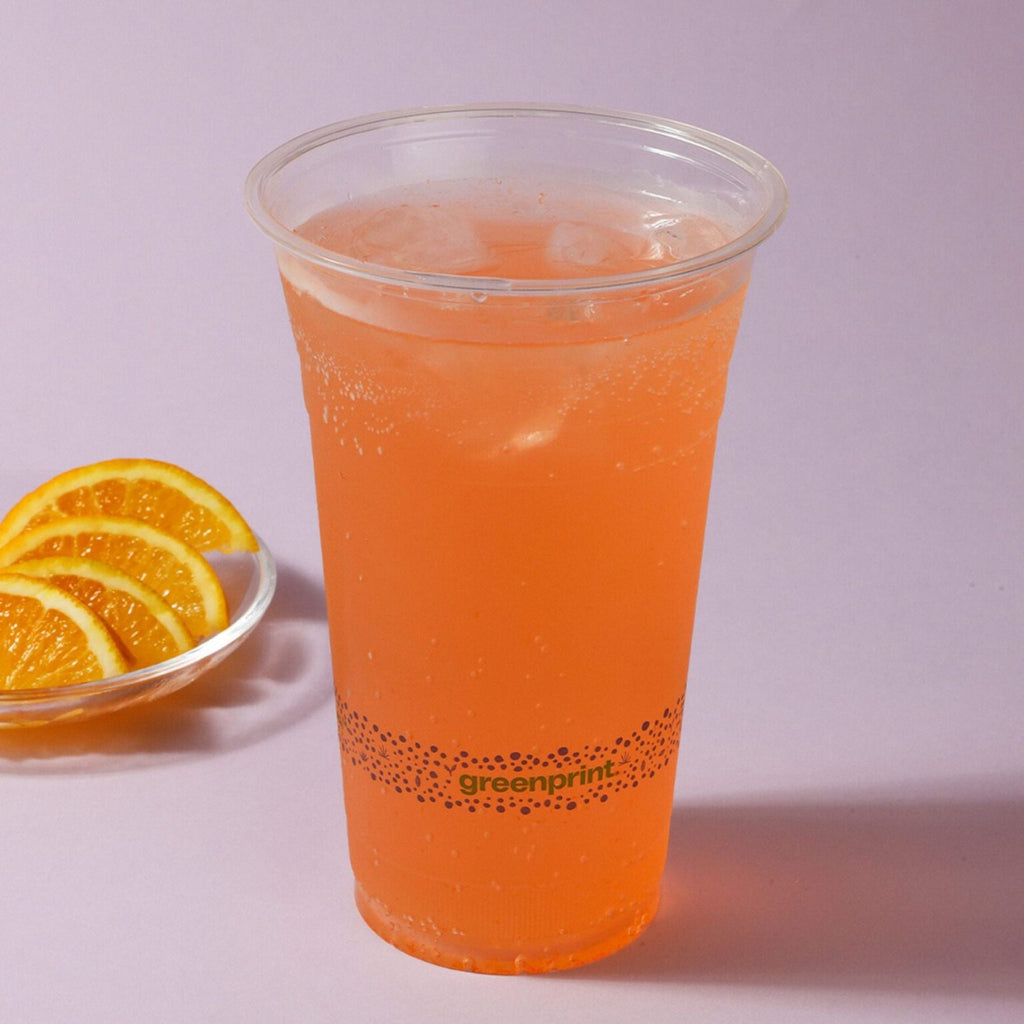Clear PLA cup with orange juice and slices of orange on a light purple background
