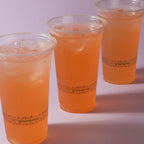 Three clear plastic cups filled with orange beverage on a white background