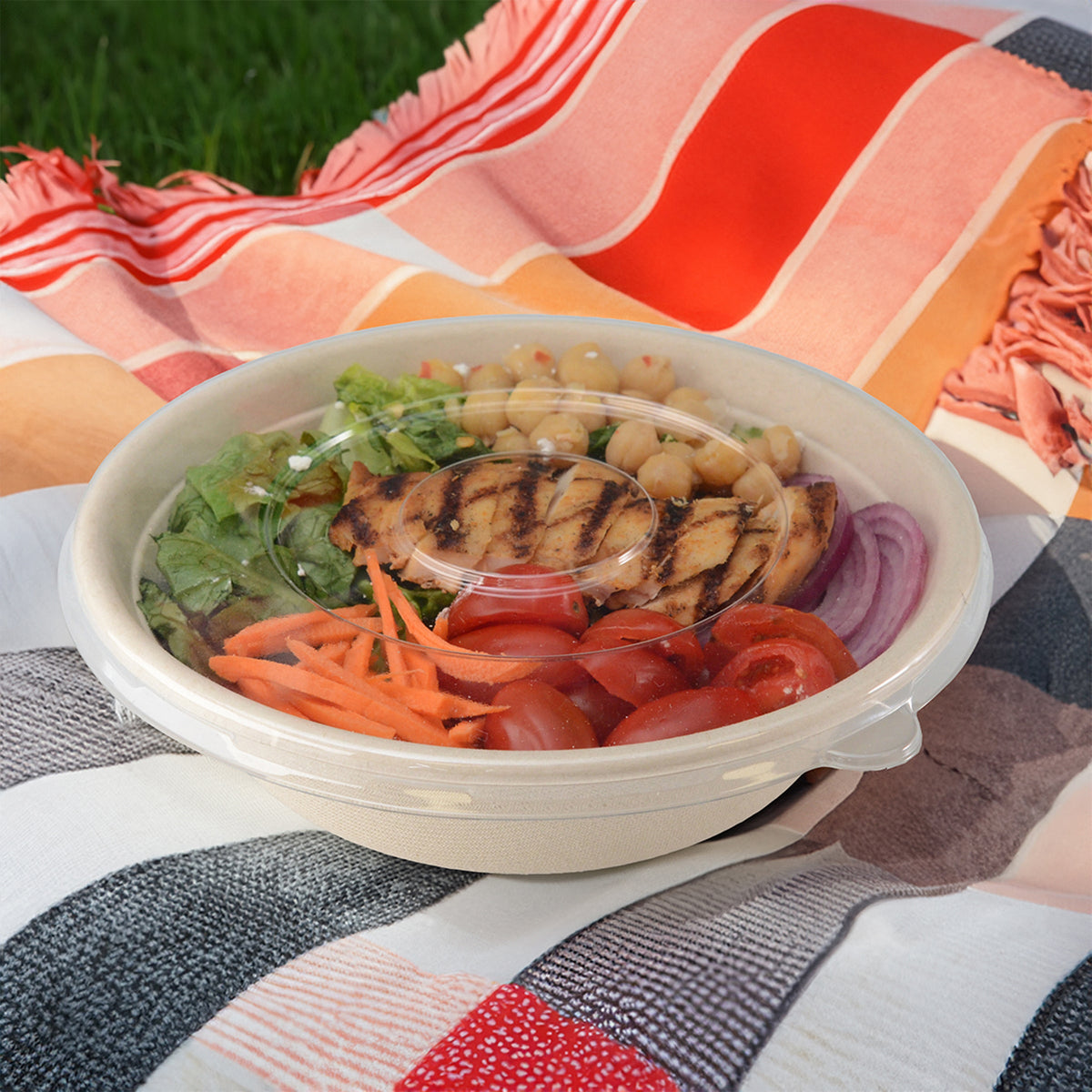Salad in a white bowl on a colorful blanket outdoors