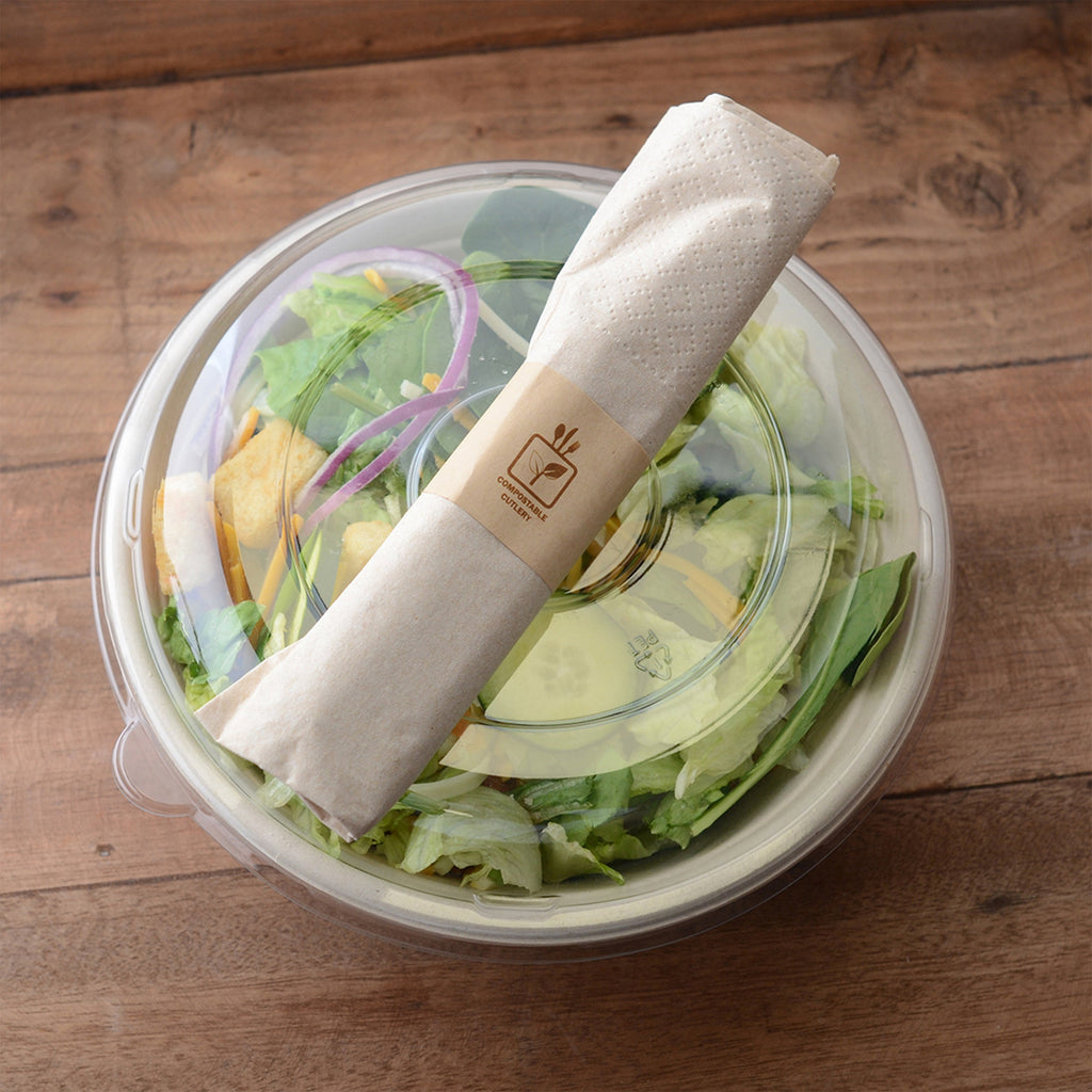 Salad in a bowl with a clear lid with a wrapped utensil on to sitting on a wooden surface