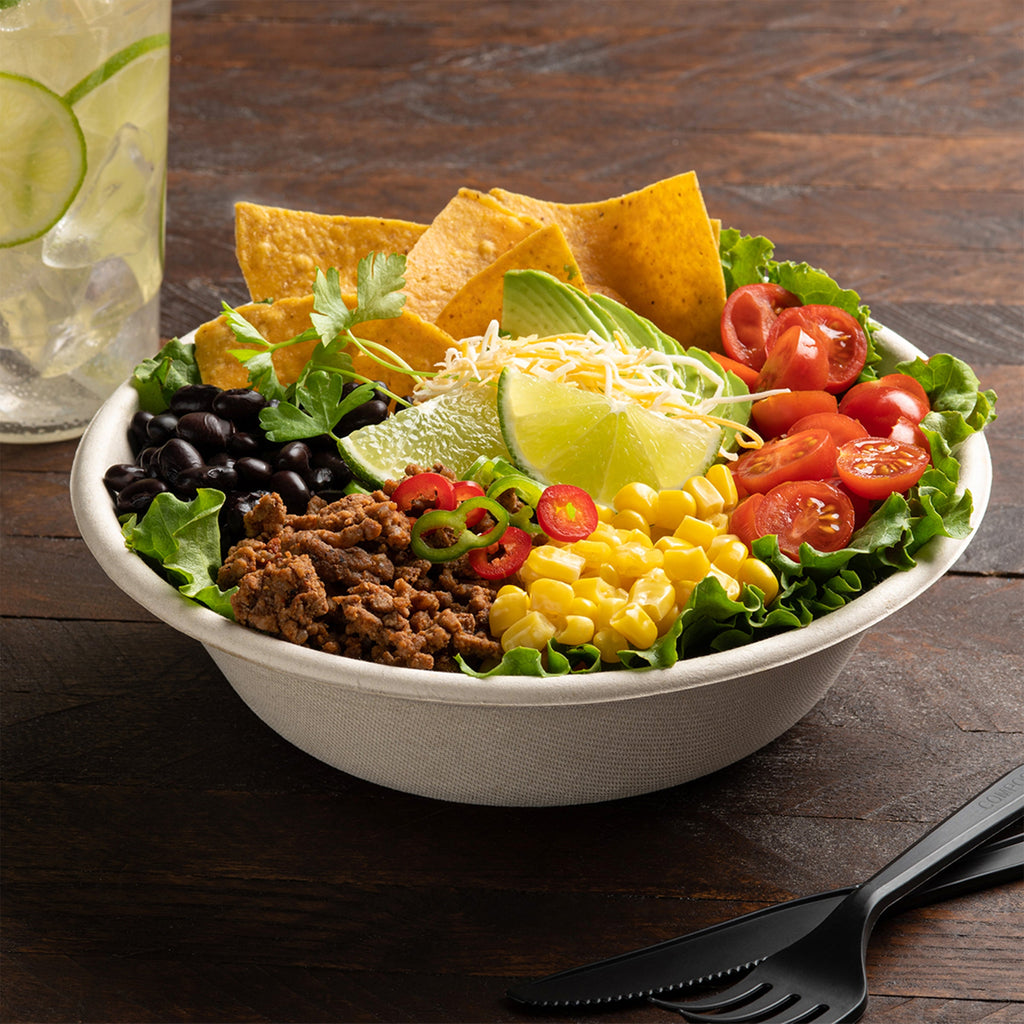 Taco salad on a white bowl with tortilla chips, lime wedges, and a glass of lemonade on a wooden table.