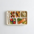 Divided lunch tray with various foods including salad, vegetables, and fish on a white background
