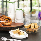 Assorted pastries and cups with hinged clear clamshell on a table with a blurred outdoor background