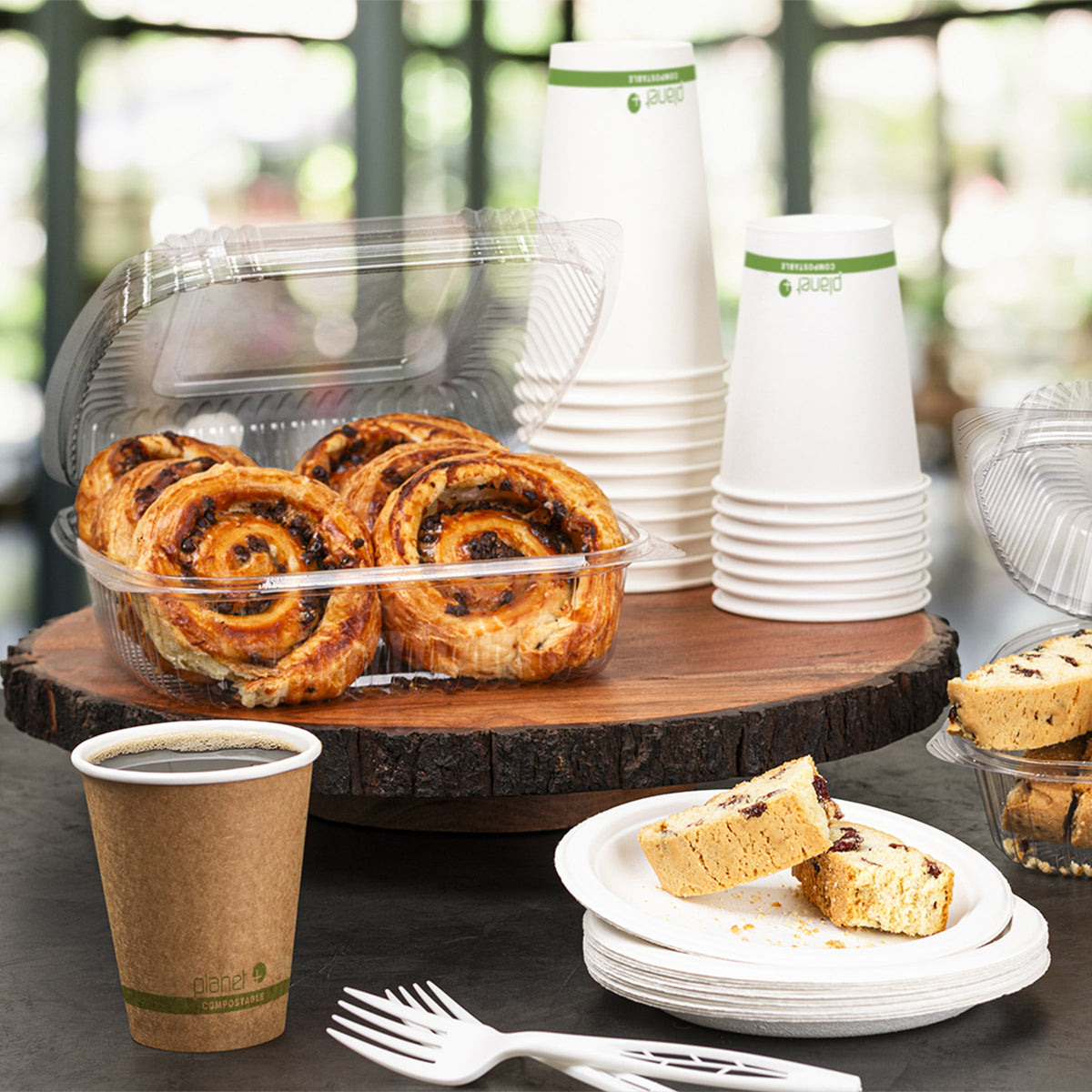 Table setting with pastries in clear containers, paper cups, and plates on a wooden surface.