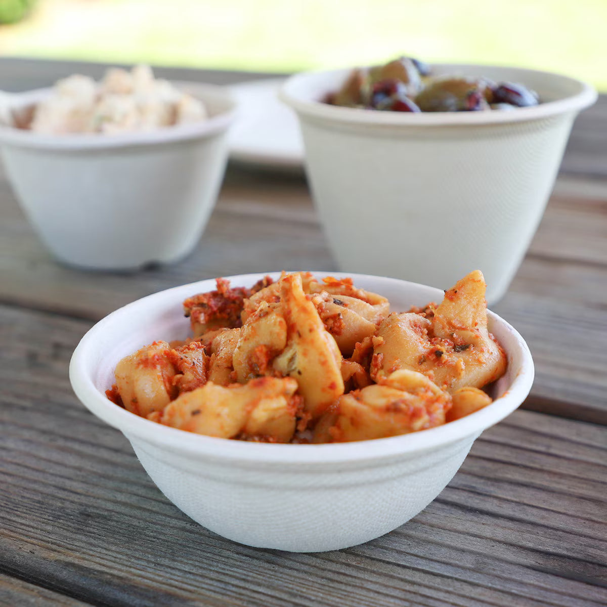 Bowl of pasta on a wooden surface with blurred bowls in the background