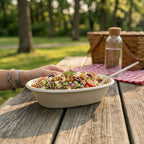 Burrito bowl of salad on a wooden table with a picnic setting in the background