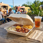 Compostable clamshell with barbecue meal on a wooden table with food trucks in the background