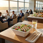 Salad in a takeout bowl with lid on a table with people in the background at an airport lounge.