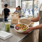 Person holding a compostable salad bowl with a lid and GPP branded items in a restaurant setting.