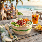 Paper bowl of salad with a drink on a wooden table by the beach