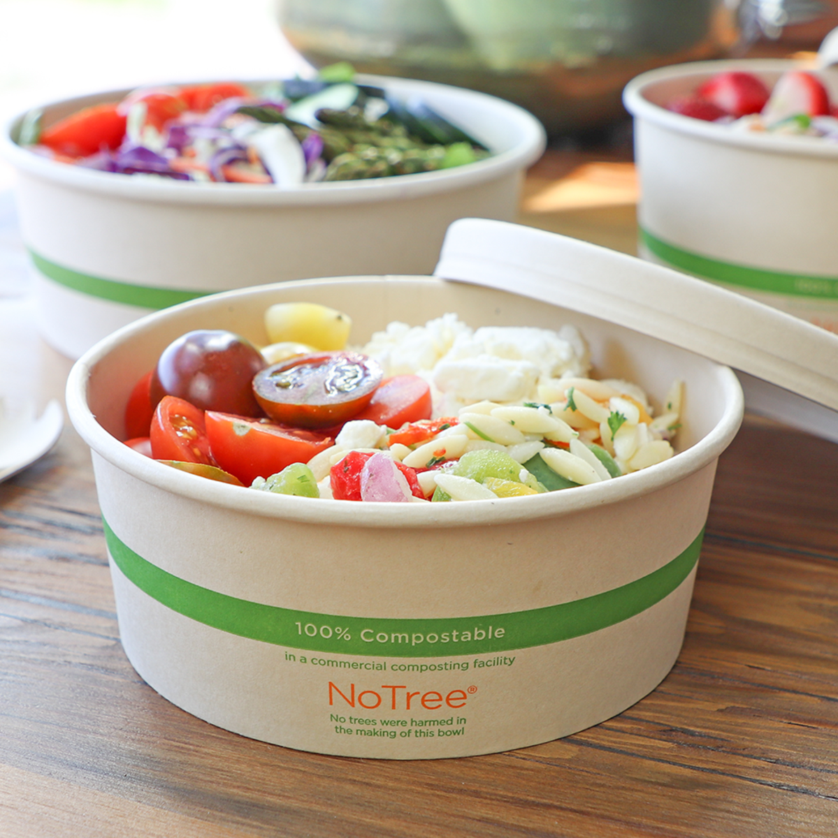 Compostable paper bowls filled with salads on a table.