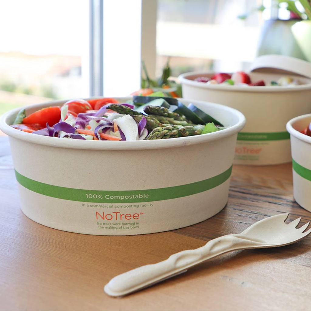 Salad in a compostable bowl with utensils on a wooden table