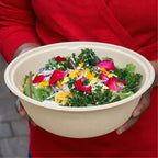 Person holding a bowl of salad with greens and colorful toppings.