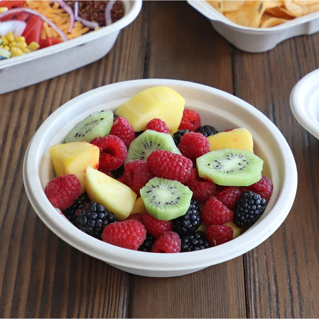 Fruit salad with kiwis, raspberries, and blackberries in a disposable tan bowl on a wooden table.