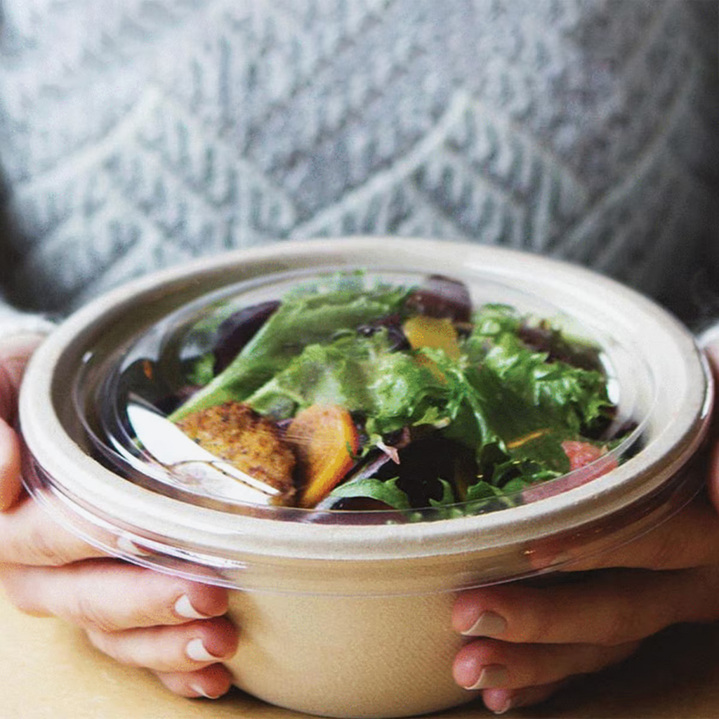 Person holding a salad in a take-out container with a blurred background