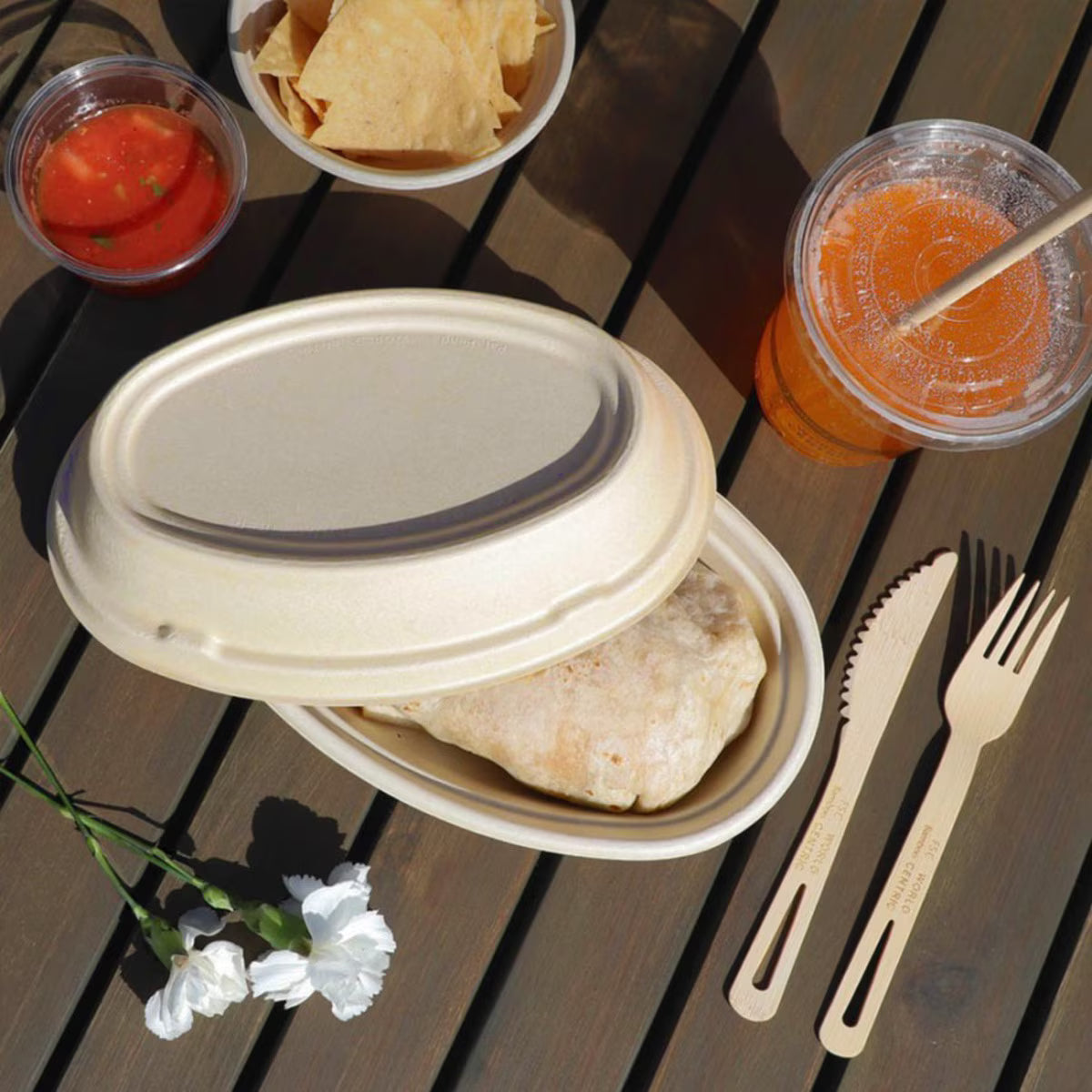 Lunch setup with tortilla, salsa, chips, juice, and cutlery on a wooden table.