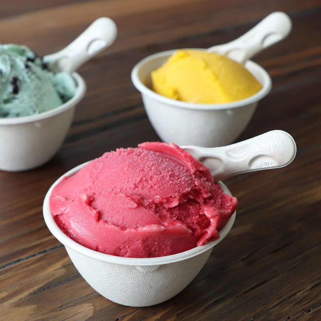 Three small bowls with scoops of colorful ice cream on a wooden surface.