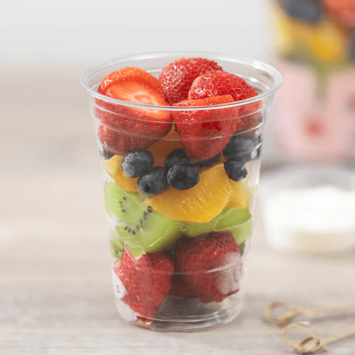 Clear plastic cup filled with assorted fruits on a light background
