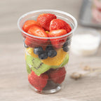 Clear plastic cup filled with sliced strawberries, blueberries, and kiwis on a wooden surface.