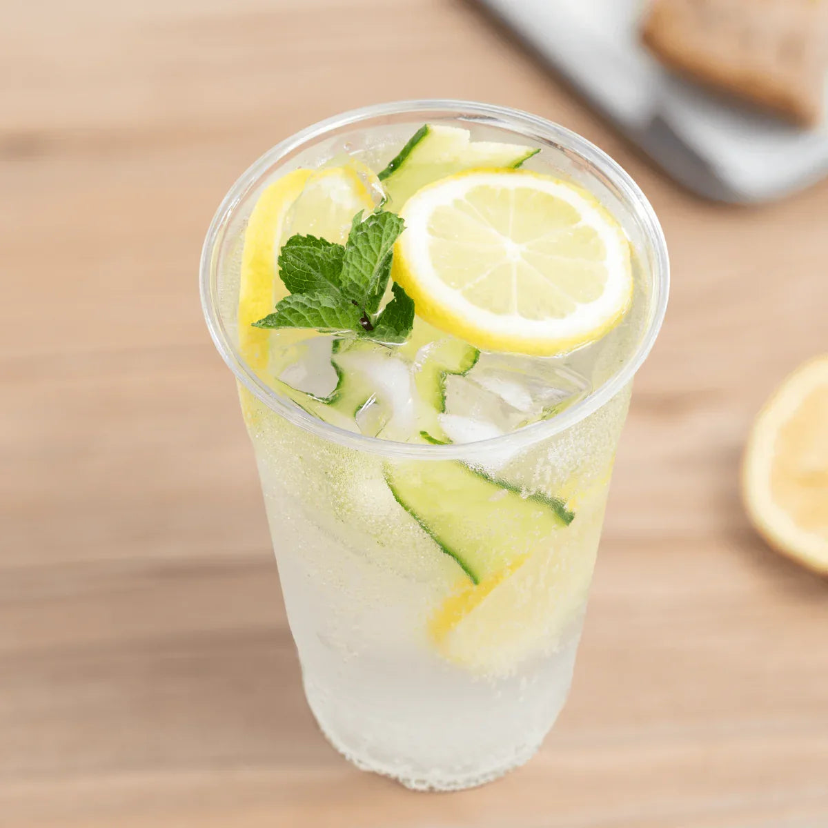Clear plastic cup filled with a lemon and cucumber infused water on a wooden surface.