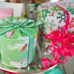 Presents wrapped in eco-friendly wrapping paper featuring snowflakes and branches with bright pink ribbon and green/white striped ribbon.