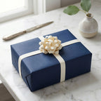 Blue gift box with a cream ribbon and bow on a marble surface.