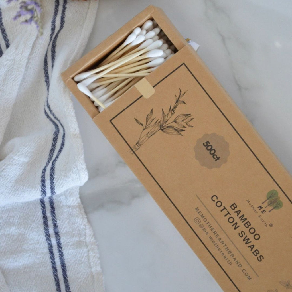 A box of cotton swabs with wooden sticks, shown open with the product visible inside. The box is kraft brown with printed text reading 'BAMBOO COTTON SWABS' and a small logo.