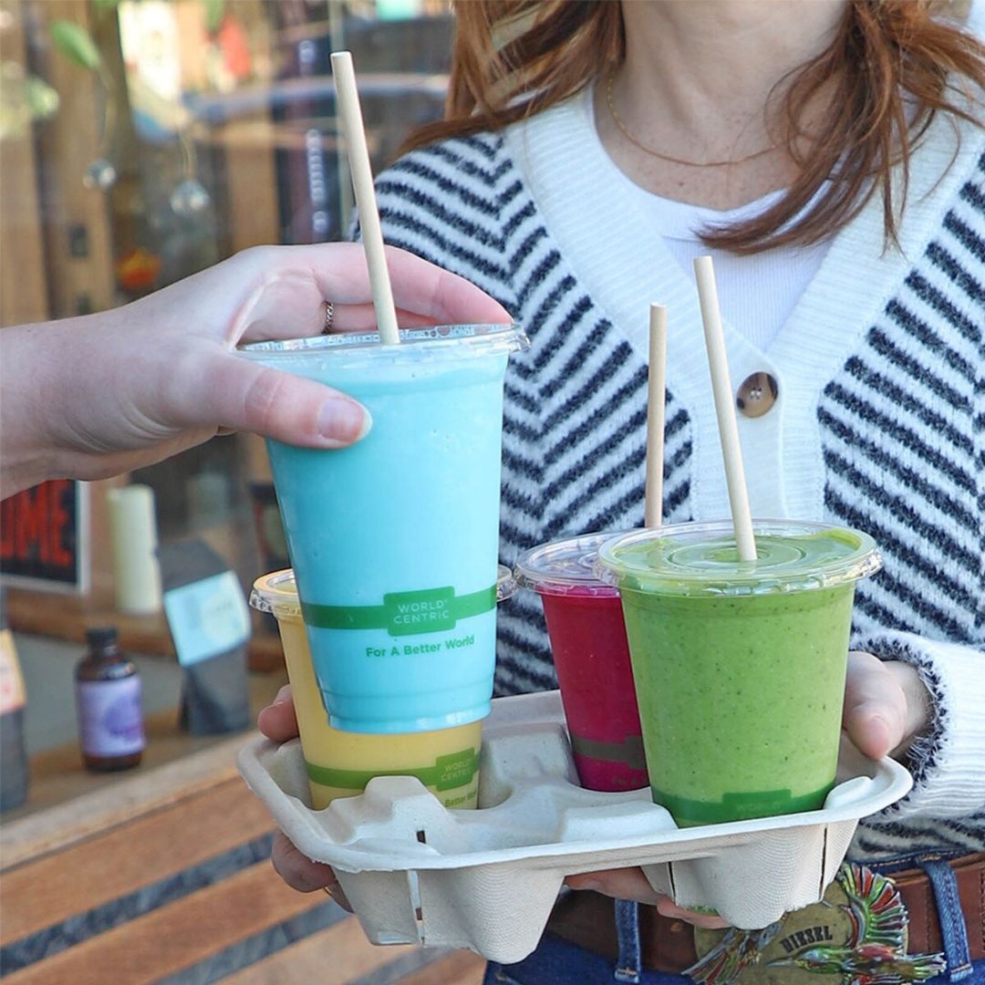 Person holding a tray with colorful smoothie cups and straws.