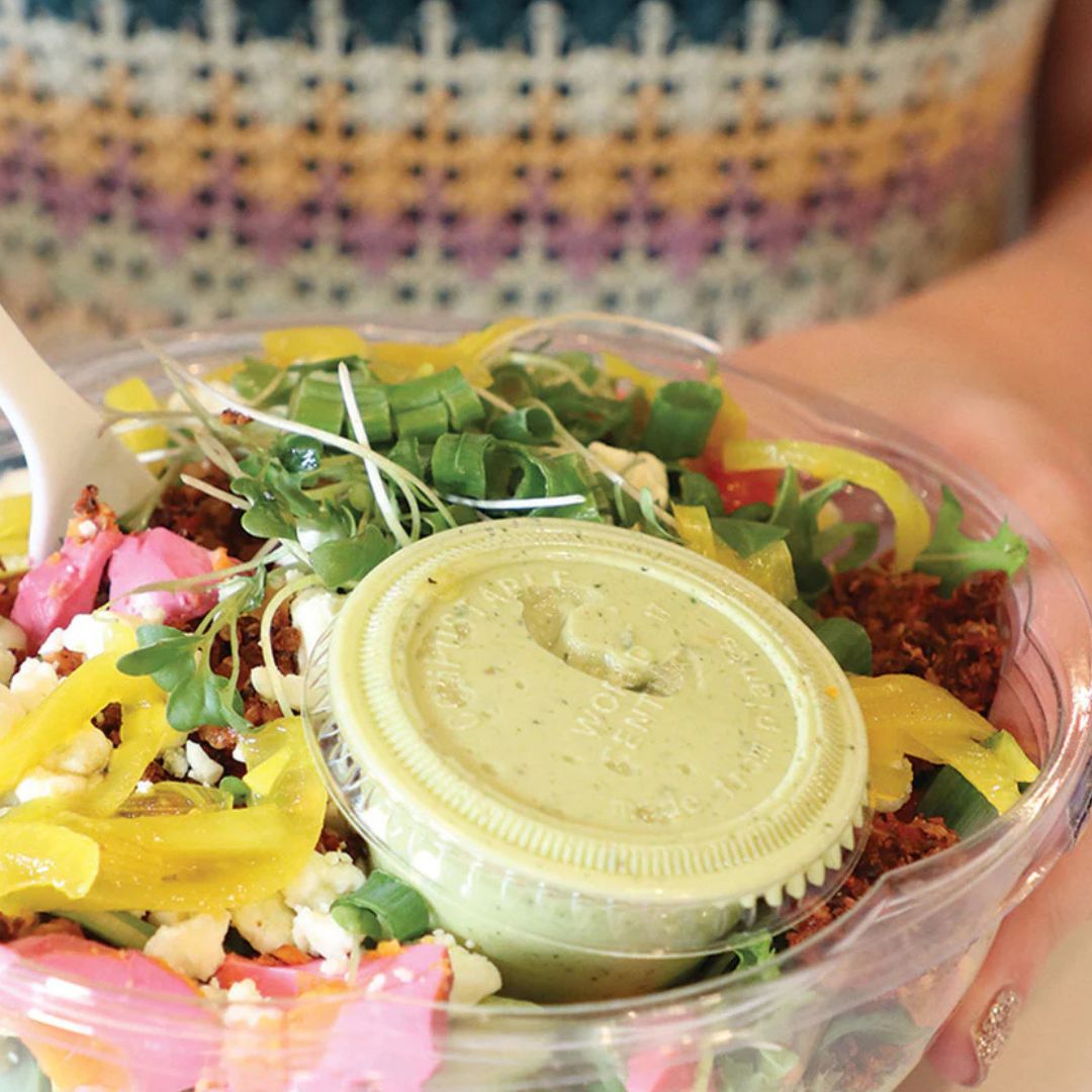 Colorful salad, with a portion cup with lid filled with dressing, held by a person.