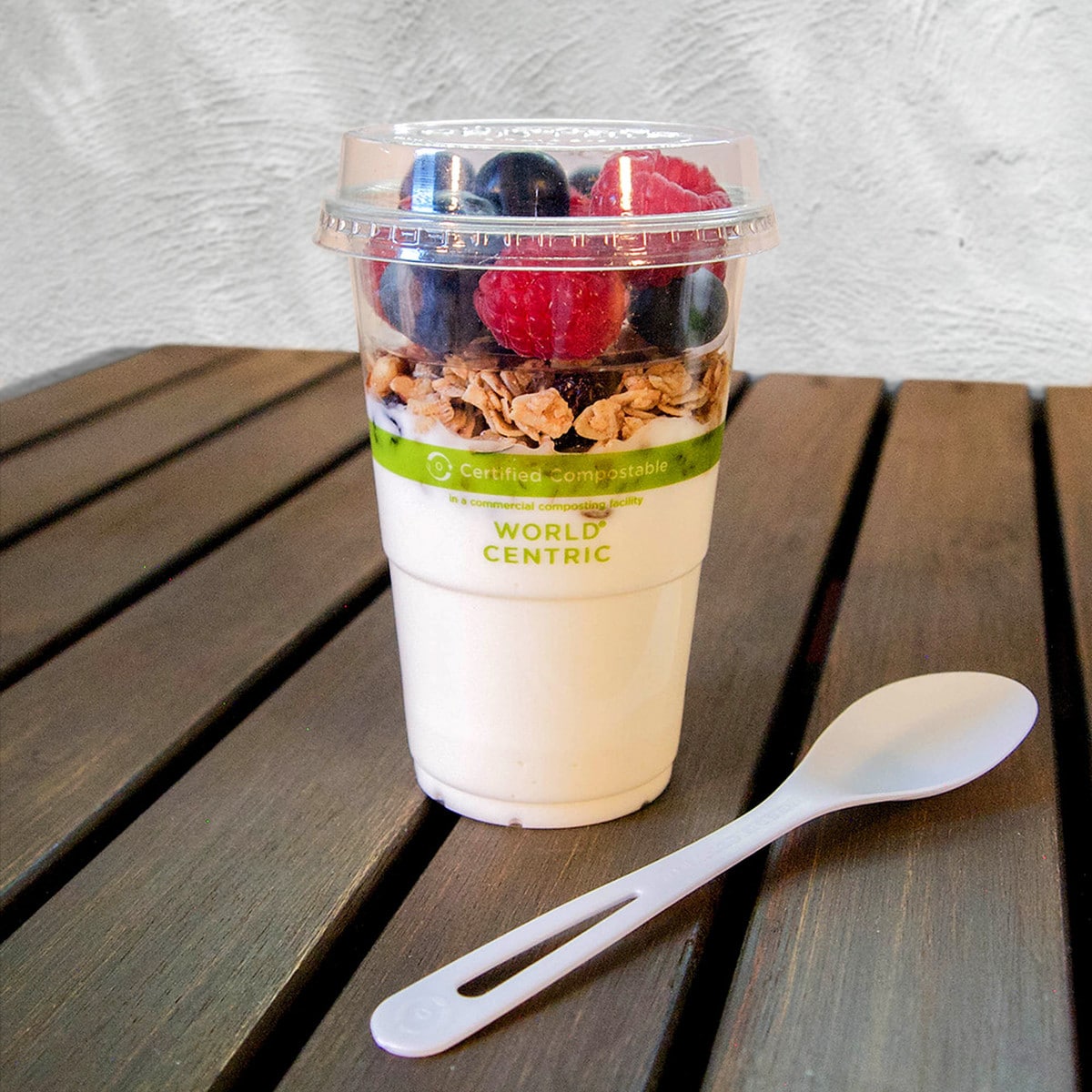 Clear compostable plastic cup with yogurt and berries on a wooden surface, featuring 'World Centric' branding.