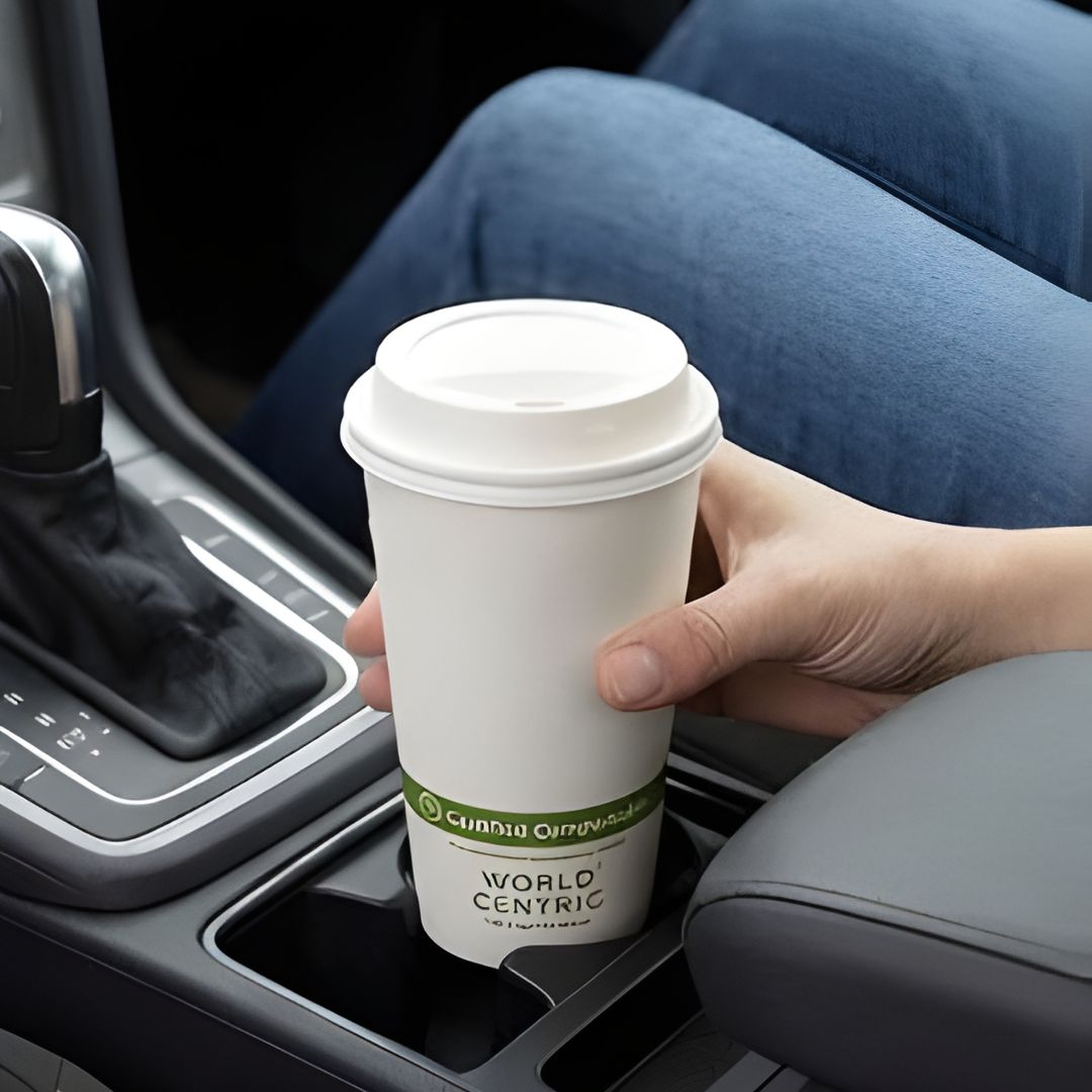 Hand holding a World Centric coffee cup in a car.