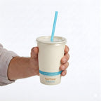 Hand holding a compostable cup with a blue straw on a white background