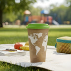 Compostable Brown paper cup with green lid on a picnic blanket in a park