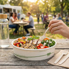 Salad bowl with a fork, water bottle, and people in the background at an outdoor setting