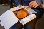White fiber takeout box with a burger and fries being held by a person enjoying their meal.