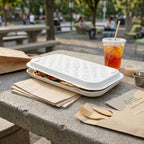 Take-out flatbread box, cup of iced tea, and wooden cutlery on a table outdoors.