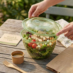 Salad in a compostable salad bowl with a lid on a wooden table outdoors.